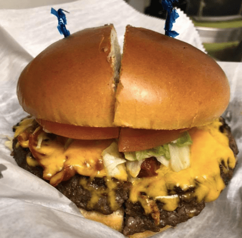 A cheeseburger with a toasted bun, melted cheese, lettuce, tomato, and a beef patty, cut in half and garnished with blue picks.