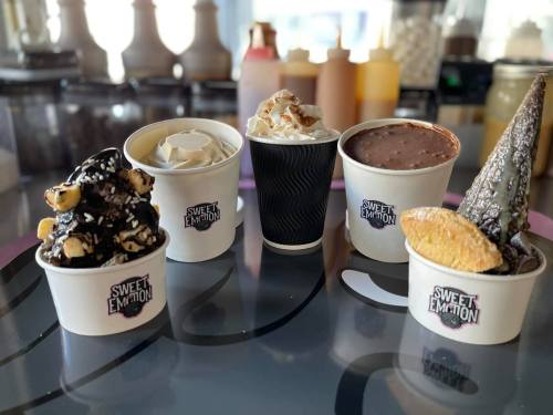 Four cups of ice cream with various toppings, displayed on a table with the logo "Sweet Emotion."