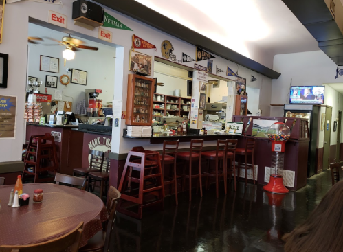 A cozy diner interior featuring a counter, seating, and various decorations, including sports memorabilia and a TV.