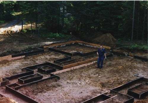 A construction worker stands on a partially excavated site with wooden forms outlining a building foundation.