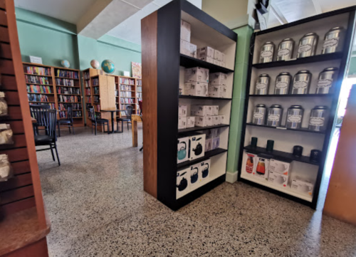 A library interior featuring shelves of products and books, with tables and chairs in the background.