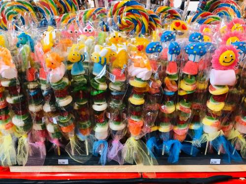 Colorful candy skewers with various shapes and designs, displayed in clear packaging at a market stall.