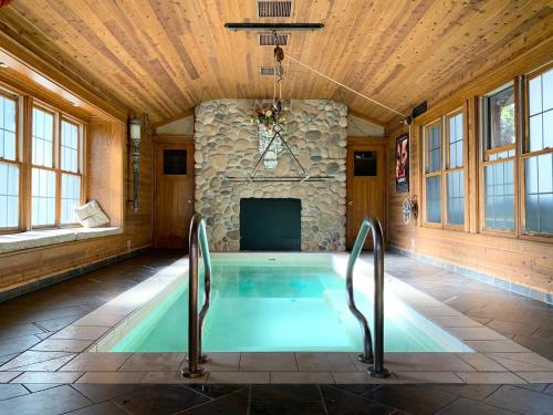 Indoor pool area with wooden walls, stone fireplace, and large windows, featuring a clear water pool and metal railings.