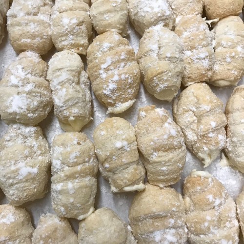 A close-up of freshly made pastries dusted with powdered sugar, arranged in neat rows on a tray.