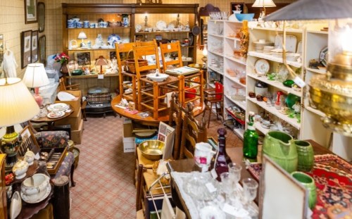 A cluttered antique shop filled with various items, including chairs, dishes, and decorative objects on shelves.
