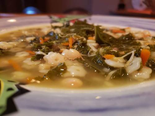 A close-up of a bowl of soup with greens, beans, and vegetables in a flavorful broth.