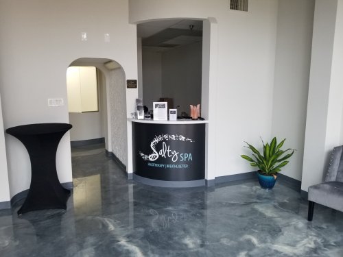 A modern spa reception area with a sleek desk, plants, and a stylish chair, featuring a welcoming atmosphere.