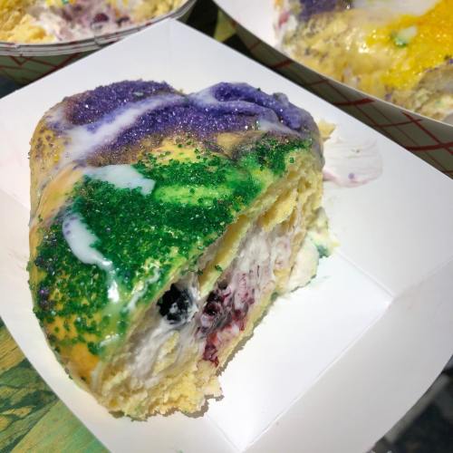 A slice of colorful king cake topped with purple, green, and yellow sprinkles and a creamy filling.