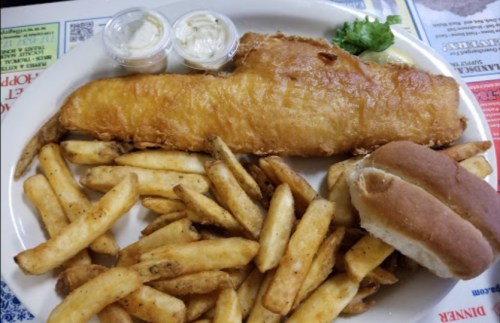 A plate of golden fried fish with tartar sauce, served with crispy fries and a soft bun on the side.
