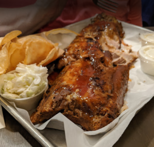 A platter featuring glazed ribs, coleslaw, and crispy potato chips on a metal tray.