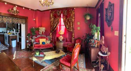 A vibrant living room with red walls, ornate furniture, plants, and decorative accents, creating a cozy atmosphere.
