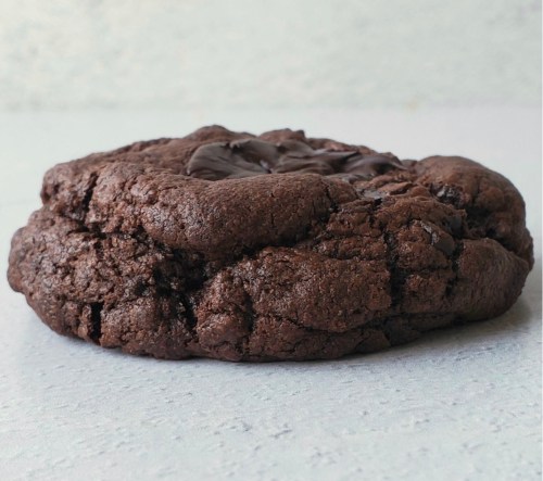 A close-up of a thick, chocolate cookie with a cracked surface and melted chocolate chunks on top.