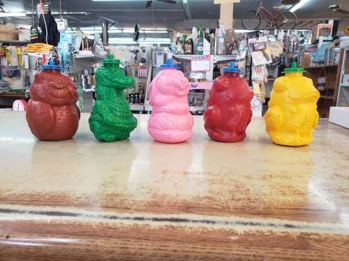 Five colorful squeeze bottles shaped like animals, arranged in a row on a wooden table in a store.