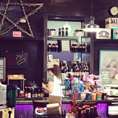 A person prepares drinks at a colorful counter with shelves of bottles and a star decoration in the background.