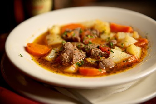 A hearty bowl of beef stew with carrots, potatoes, and herbs in a rich broth, served in a white dish.