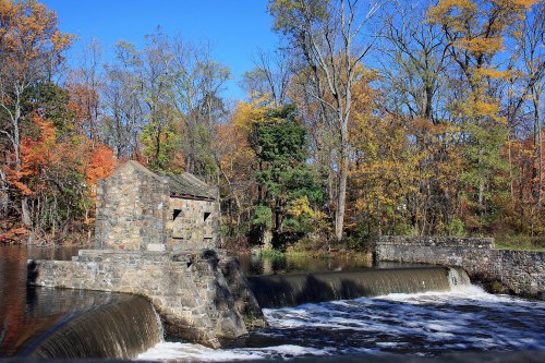 A stone structure beside a waterfall, surrounded by colorful autumn trees under a clear blue sky.