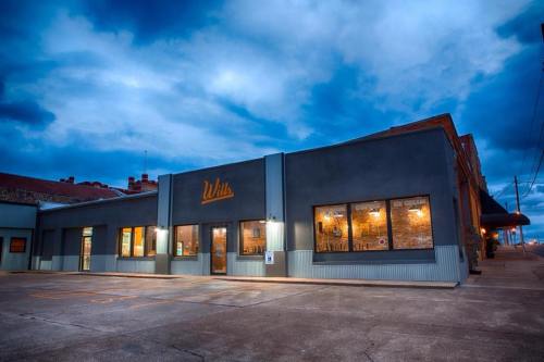 A modern building with large windows, featuring the name "Wils" illuminated against a cloudy evening sky.