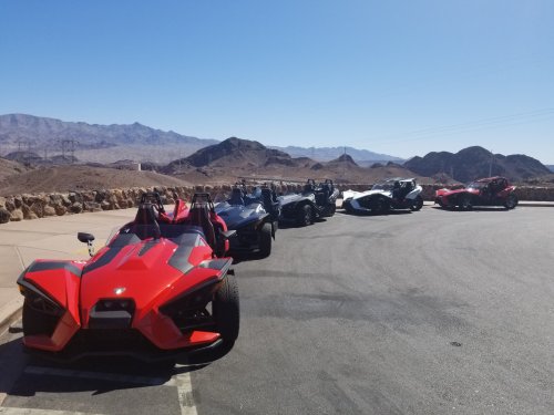 A row of colorful three-wheeled vehicles parked against a mountainous desert backdrop under a clear blue sky.