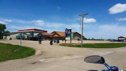 A gas station and convenience store on a sunny day, with motorcycles parked outside and a clear blue sky.