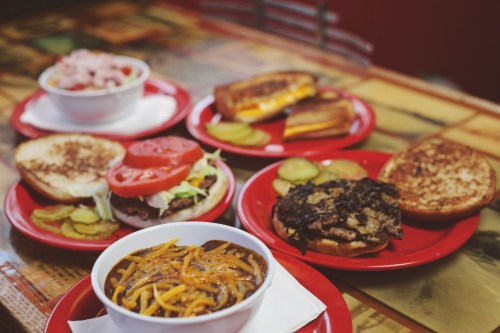 A spread of comfort food on red plates, including a burger, grilled cheese, and a bowl of spaghetti with sauce.