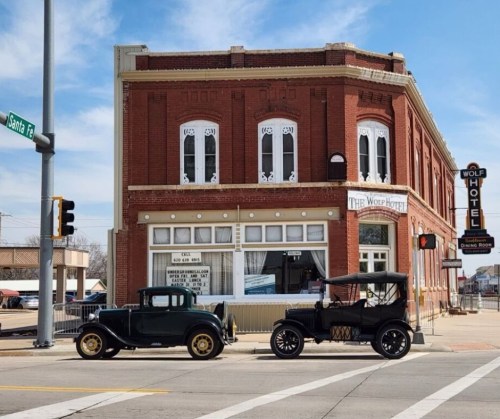 Historic brick building with "Wolf Hotel" sign, featuring two vintage cars parked in front on a sunny day.