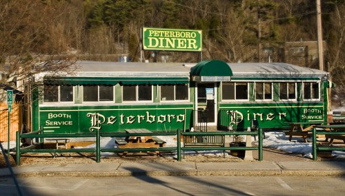 A green and white diner with "Peterboro Diner" signage, featuring outdoor seating and a snowy landscape.