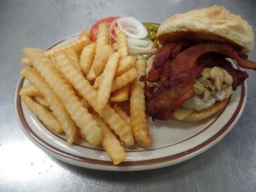 A plate with a bacon sandwich topped with onions and pickles, accompanied by a side of crinkle-cut fries.