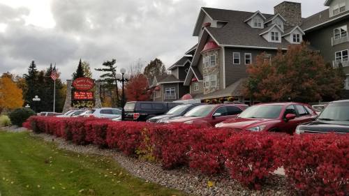 A hotel with a stone facade and red foliage in front, surrounded by parked cars and autumn trees under a cloudy sky.
