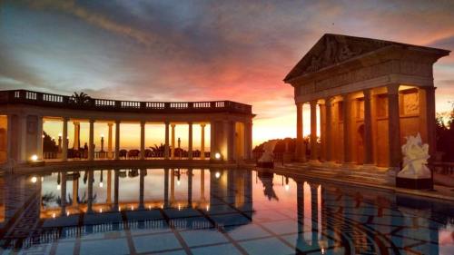 A serene sunset over a grand pool with classical architecture and reflections in the water.