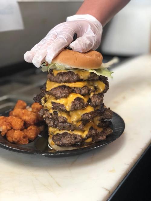 A towering burger with multiple beef patties and melted cheese, served with a side of tater tots.