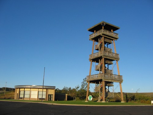 A tall wooden observation tower next to a modern building against a clear blue sky.