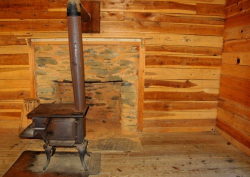 A rustic wood stove in a log cabin, with a stone fireplace and wooden walls.