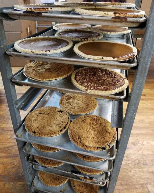 A metal rack filled with various pies, including pecan and pumpkin, in a bakery setting.