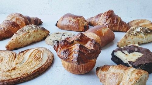 A variety of baked goods including croissants, pastries, cookies, and brownies arranged on a light surface.