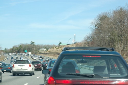 Traffic jam on a highway with multiple vehicles and trees lining the road under a clear blue sky.