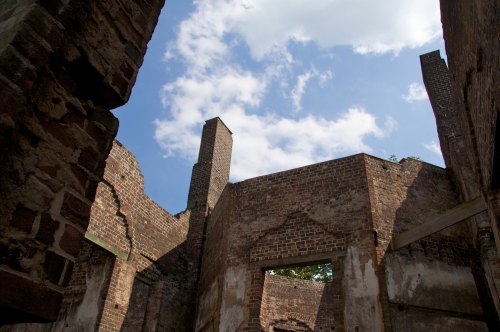 View of the sky through the ruins of a brick building, with clouds and remnants of walls visible.