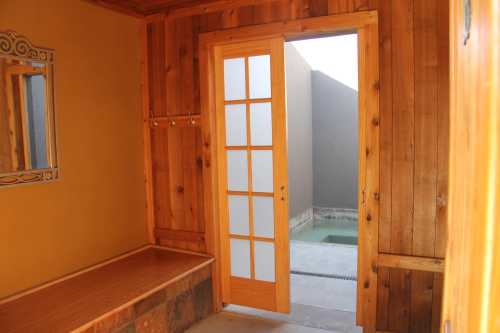 A wooden interior with a bench, mirror, and a door leading to an outdoor area with a pool.