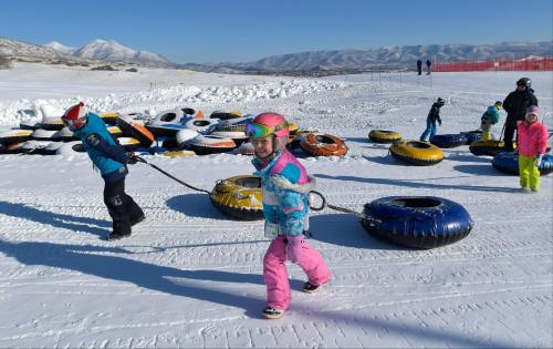Children playing in the snow, pulling inflatable tubes, with snowy mountains in the background.