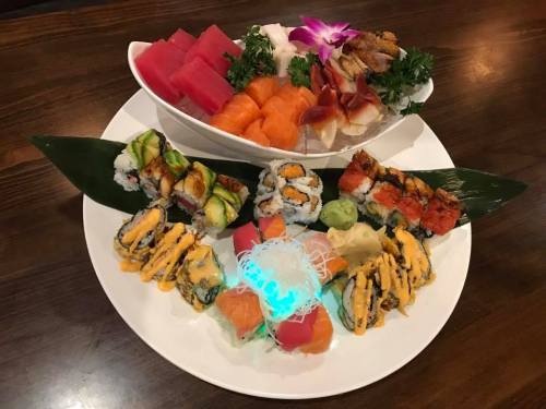 A beautifully arranged sushi platter featuring various rolls, sashimi, and garnishes on a wooden table.