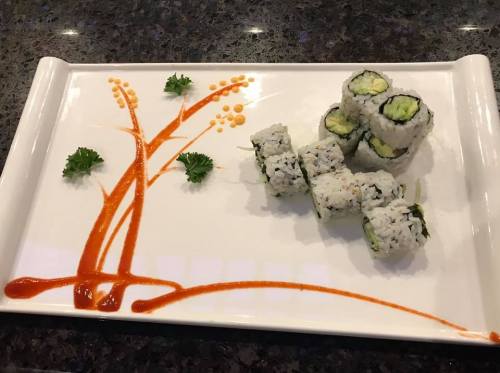 A decorative plate with sushi rolls and a tree design made of sauce and garnishes.