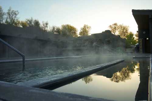 A serene hot spring with steam rising, surrounded by trees and a tranquil atmosphere at sunrise.