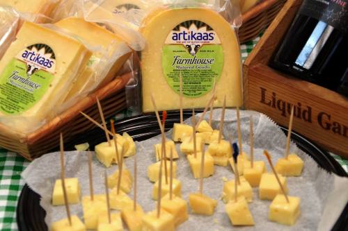 A platter of cubed Farmhouse Gouda cheese with toothpicks, surrounded by cheese packages and a bottle of wine.
