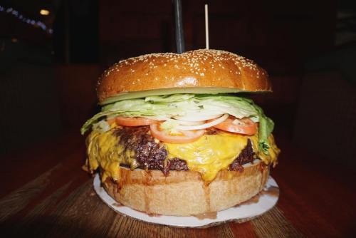 A large cheeseburger with lettuce, tomato, and a sesame seed bun, served on a wooden table.