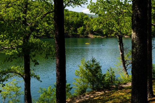 A serene lake surrounded by lush green trees, with two kayakers paddling in the calm water.