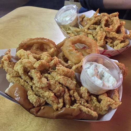 Two trays of fried food: one with crispy onion rings and the other with fried strips, served with dipping sauce.