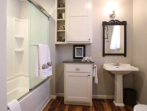 A modern bathroom featuring a shower, sink, cabinet, and decorative items on the wall. Warm wood flooring completes the look.