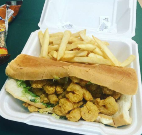 A takeout container with a shrimp sandwich and a side of French fries.