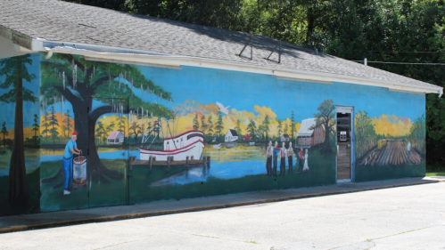 Colorful mural depicting a scenic river, a boat, and people by a tree, showcasing local life and nature.