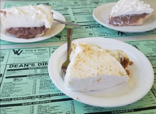 Three slices of pie on a green menu: chocolate cream, banana cream, and coconut cream, with a fork on the plate.