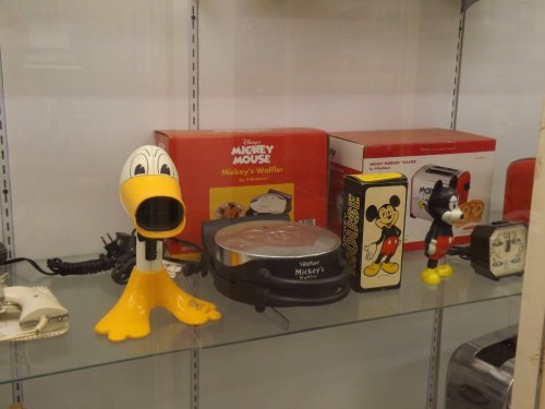 A display case featuring Disney-themed kitchen appliances, including a Donald Duck waffle maker and Mickey Mouse items.